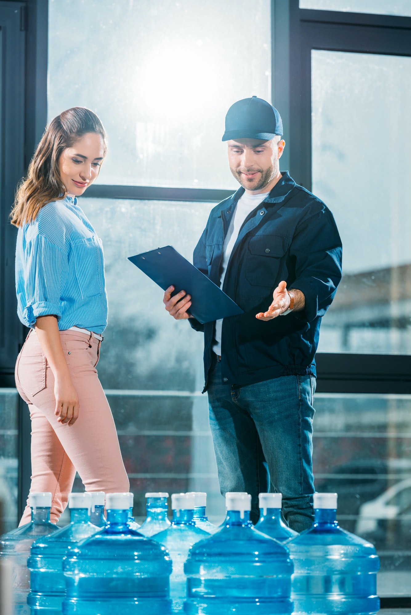 courier-with-clipboard-and-woman-looking-at-delivered-water-bottles.jpg